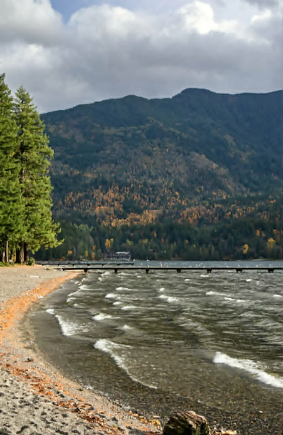 The shore of Cultus Lake — Swìlhcha — with evergreens, the dock and mountains behind